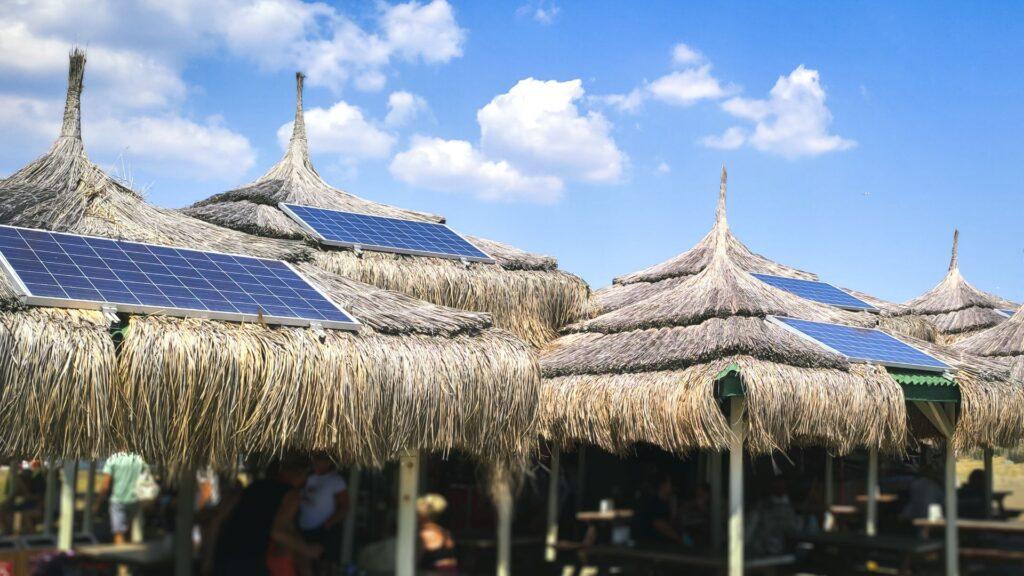 Blauer tropischer Himmel und authentische traditionelle polynesische Strohdachhäuser mit umweltfreundlicher Nutzung von Solarzellen. Blick auf den Strand mit einem Gebäude mit Solarzellen auf dem Dach. 