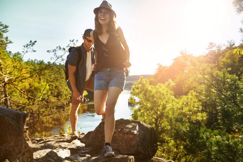 Natur, Wandern und Paar zu Fuß mit Fluss, blauer Himmel und Abenteuerurlaub auf dem Lande. Trekking, Mann und Frau auf nachhaltige Reise Urlaub zusammen im Park mit Bäumen, Wasser und im Freien Datum