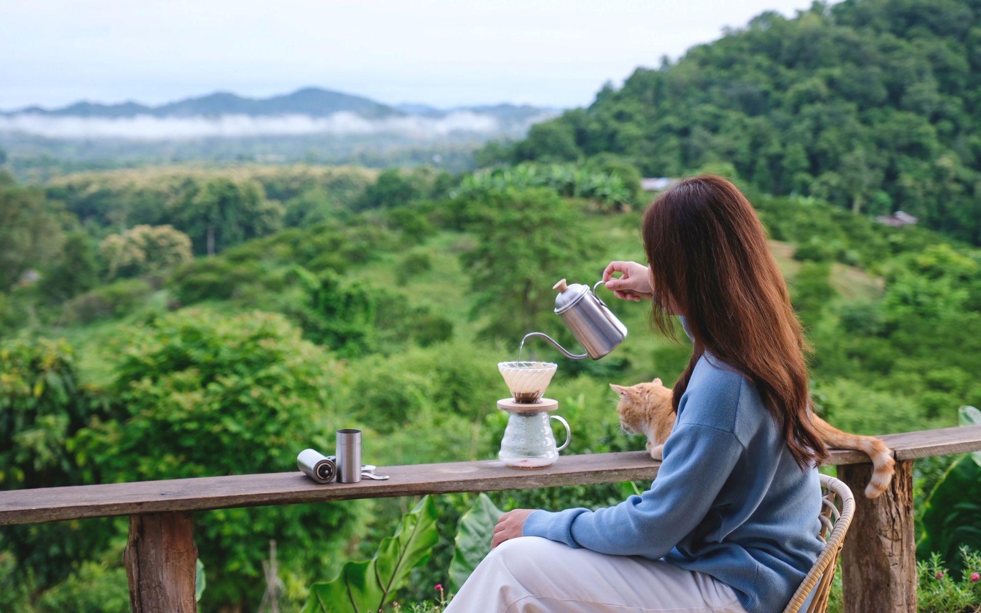 Frau genießt Kaffee auf einer Terrasse mit Blick in die Natur des Bayerischen Waldes.