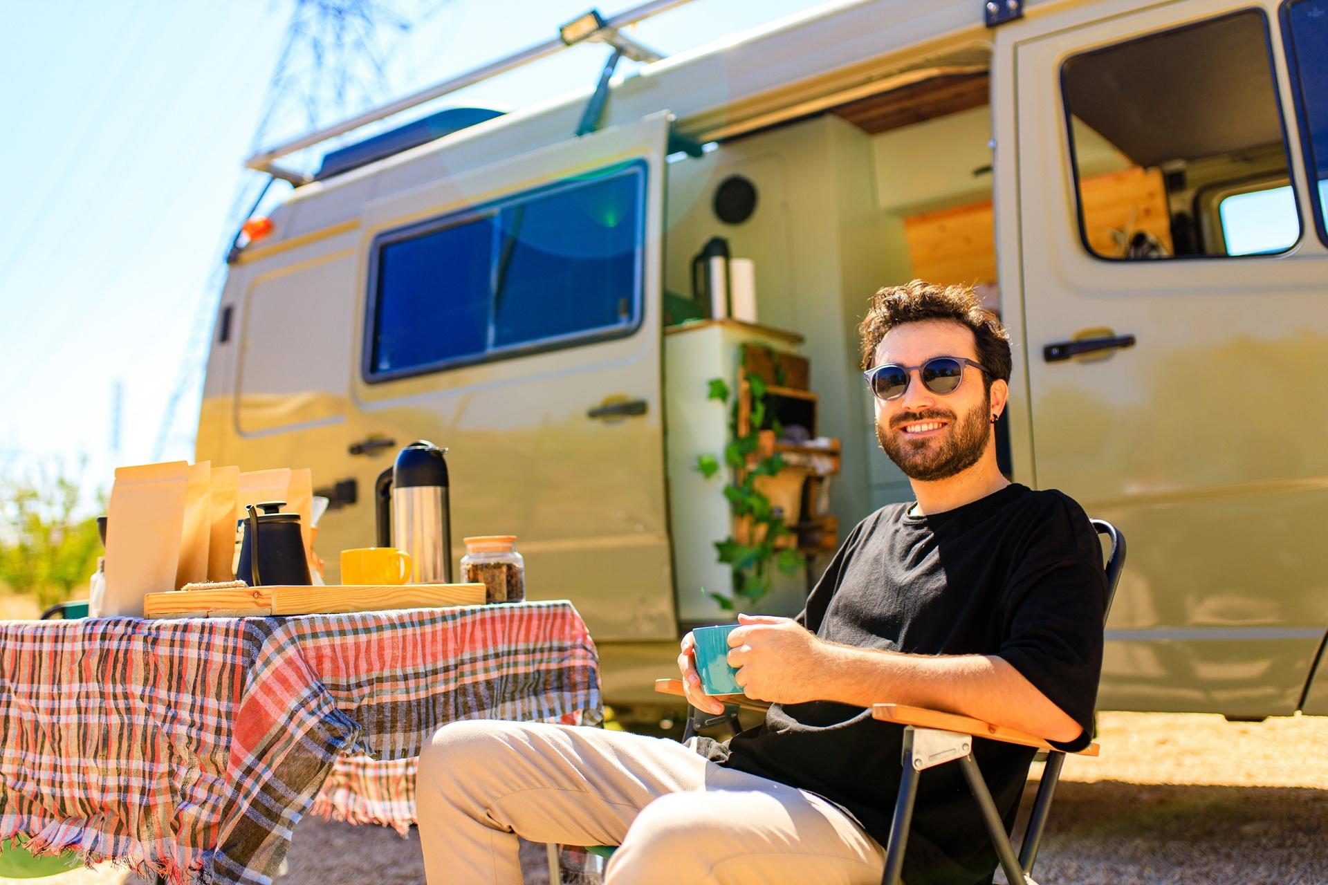 Mann sitzt mit Kaffee vor Campervan | Elf Bar Elfa